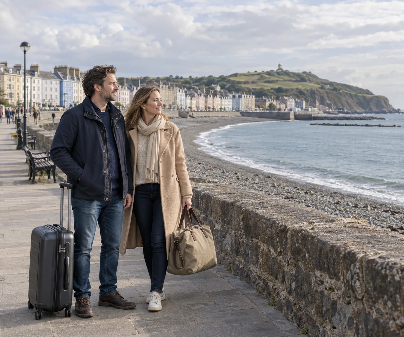 Two travellers with luggage looking across a curved bay from the seafront promenade
