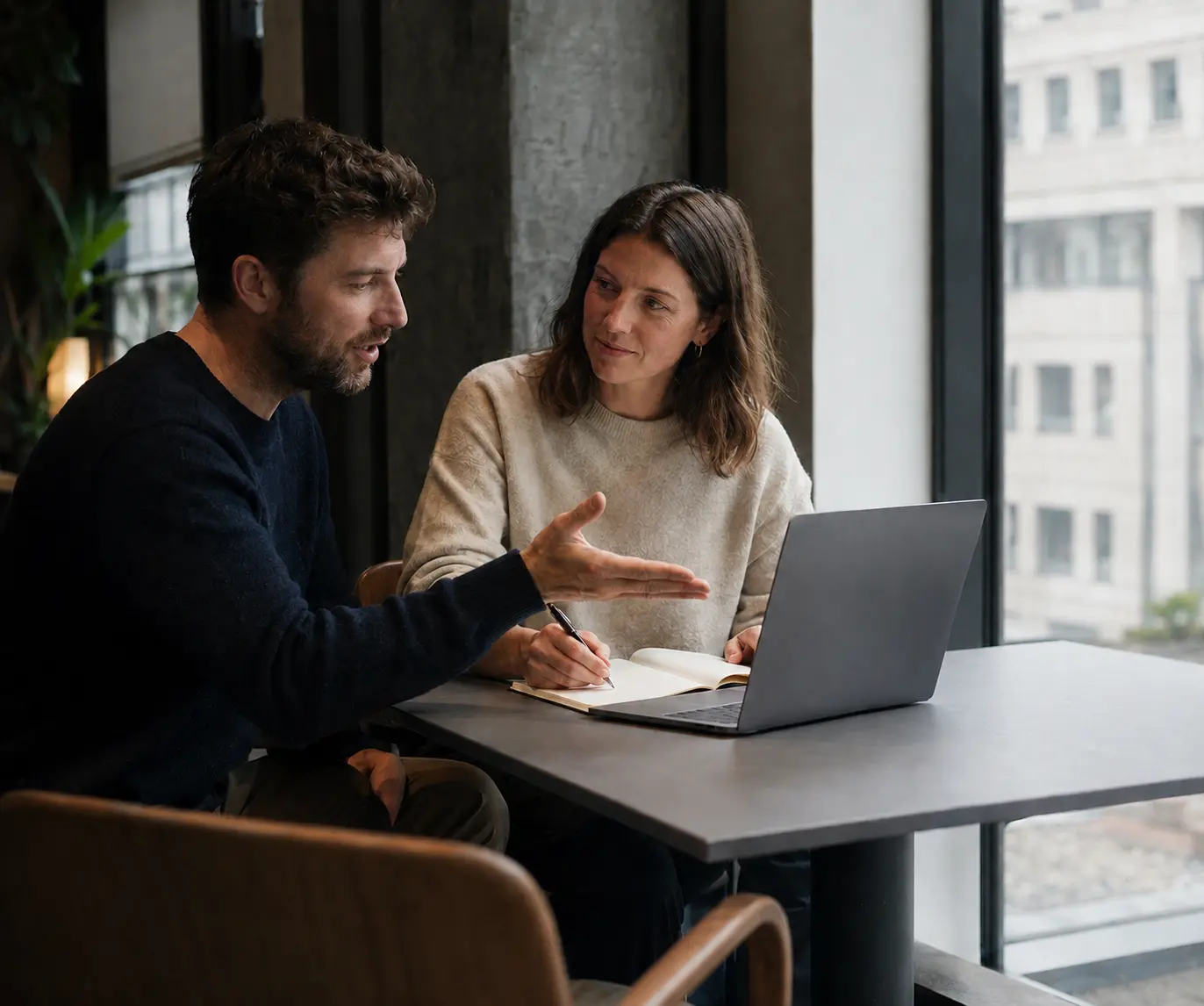 Two people discussing travel plans with a laptop and notes