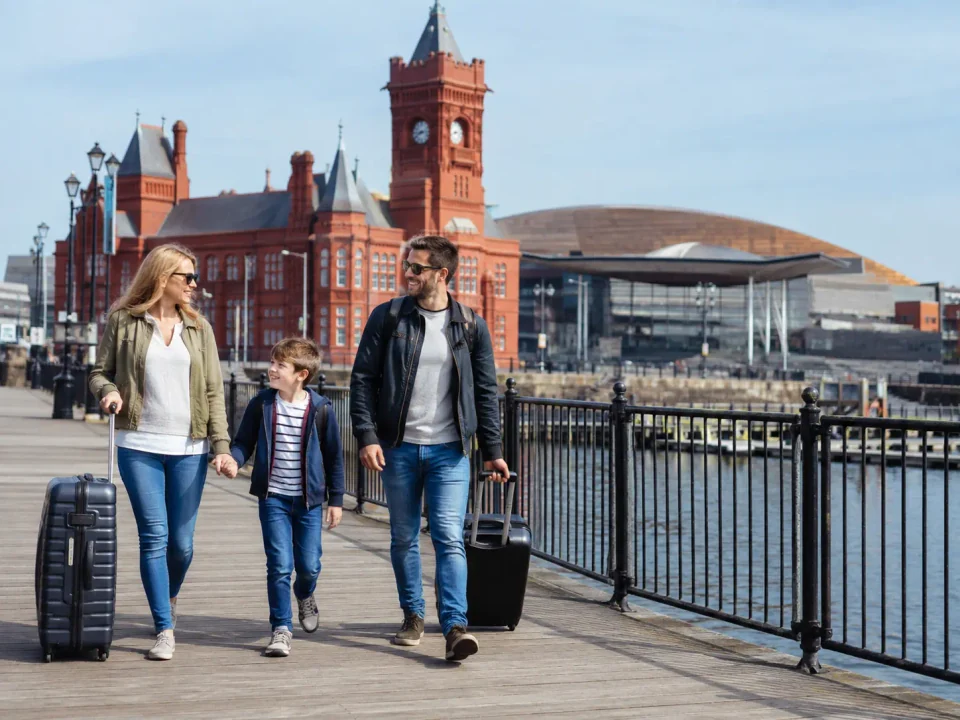 Family travellers walking along Cardiff Bay beside the red-brick Pierhead building