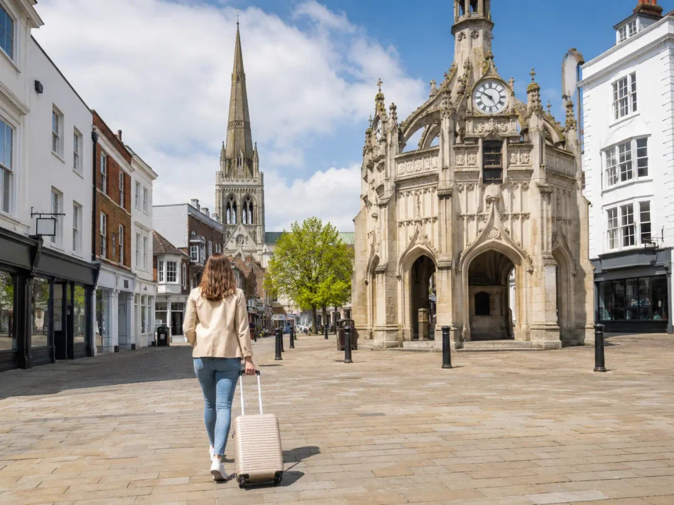 Traveller with a suitcase beside Chichester Market Cross and the cathedral spire