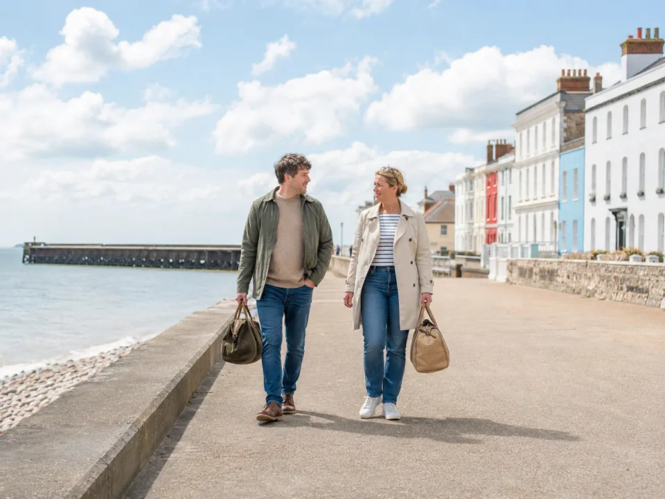 Travelling couple carrying weekend bags on Deal seafront beside the pier