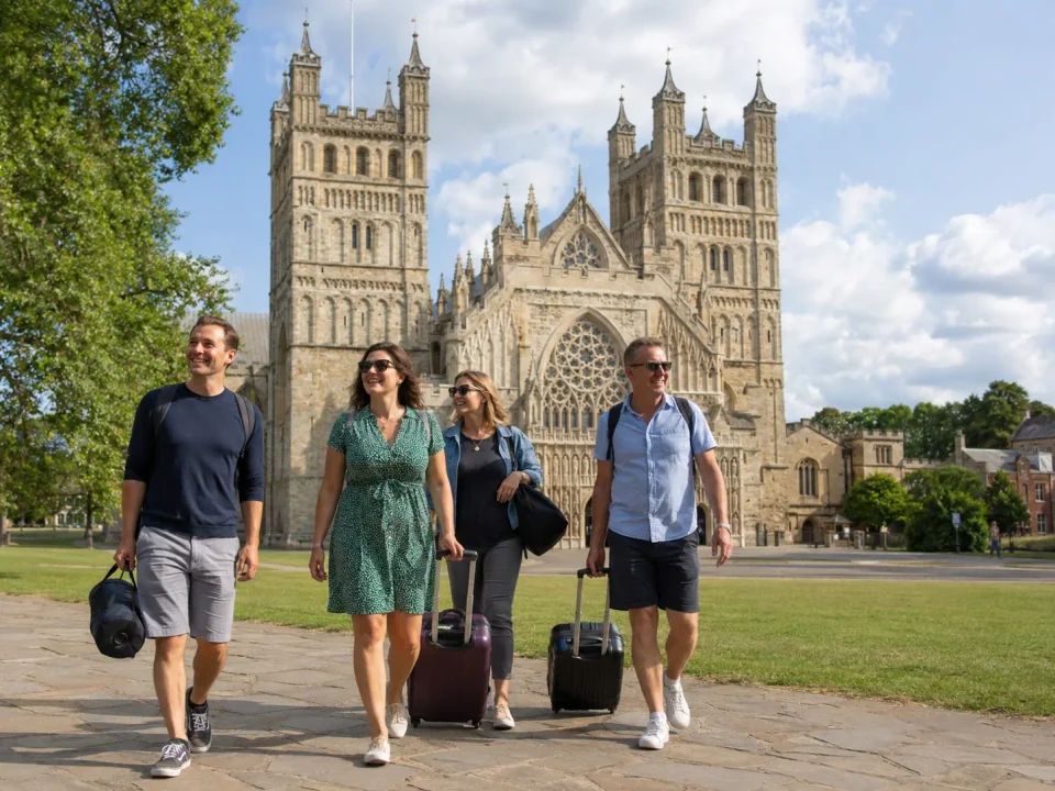 Family travellers with luggage walking beside Exeter Cathedral