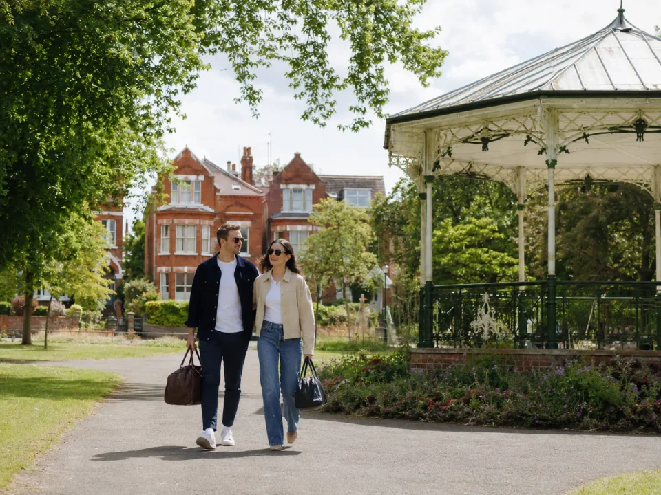 Travelling couple with luggage beside a park bandstand in Finchley