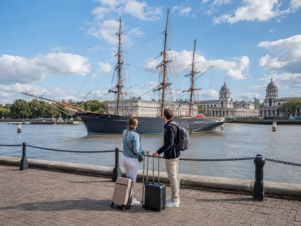 Travellers with luggage beside the historic clipper and Old Royal Naval College in Greenwich