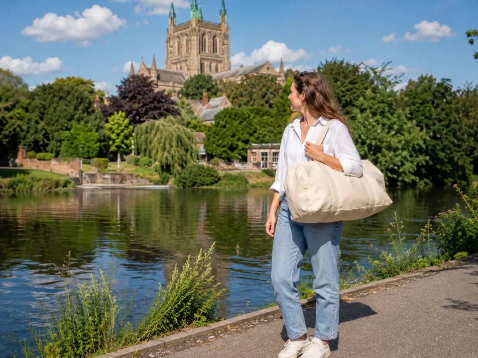 Woman traveller with a weekend bag beside the River Wye and Hereford Cathedral