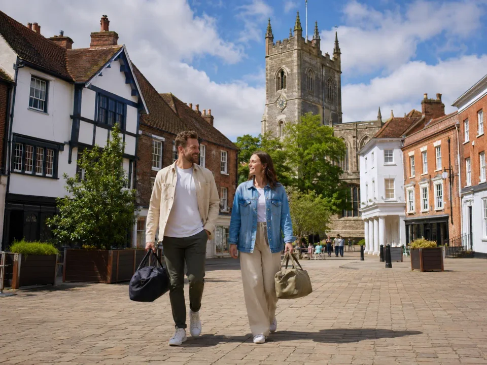 Travelling couple carrying weekend bags through Hitchin market square