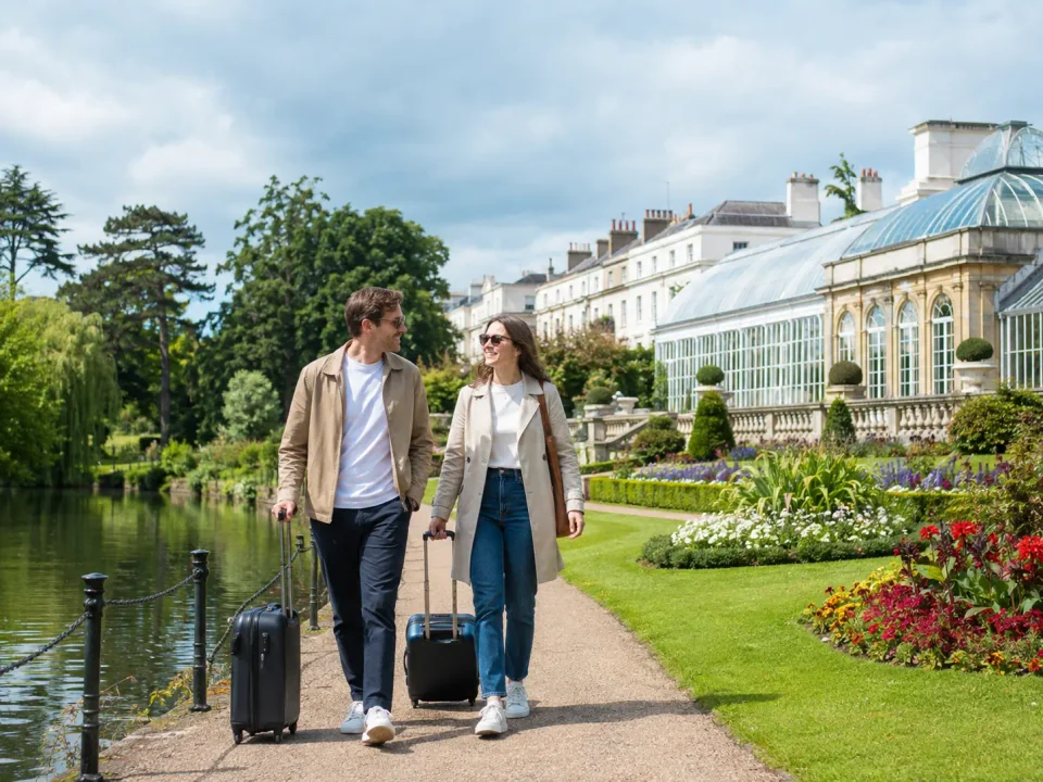 Travelling couple with suitcases in Jephson Gardens beside the glasshouse in Leamington Spa
