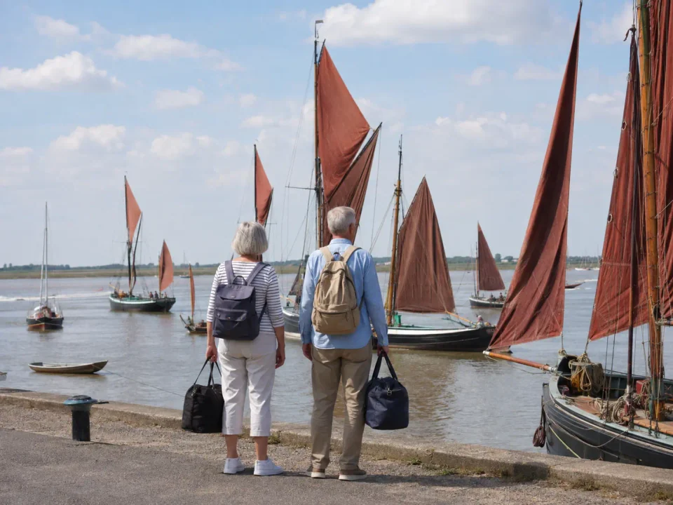 Older travellers with overnight bags admiring Thames sailing barges at Maldon