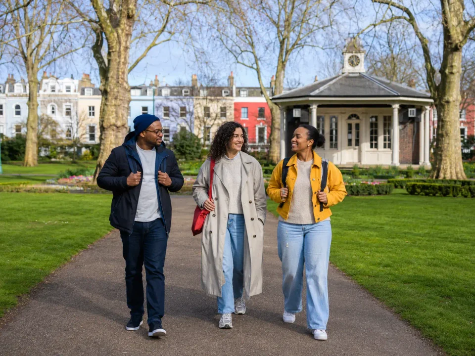 Friends with travel bags walking through Peckham Rye Park and Common