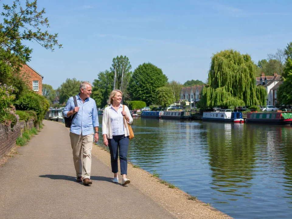 Older travellers walking beside the River Thames and moored boats in Shepperton