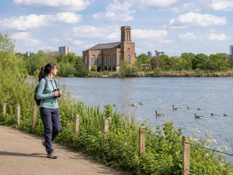 Visitor with binoculars beside the reservoir and engine house at Walthamstow Wetlands