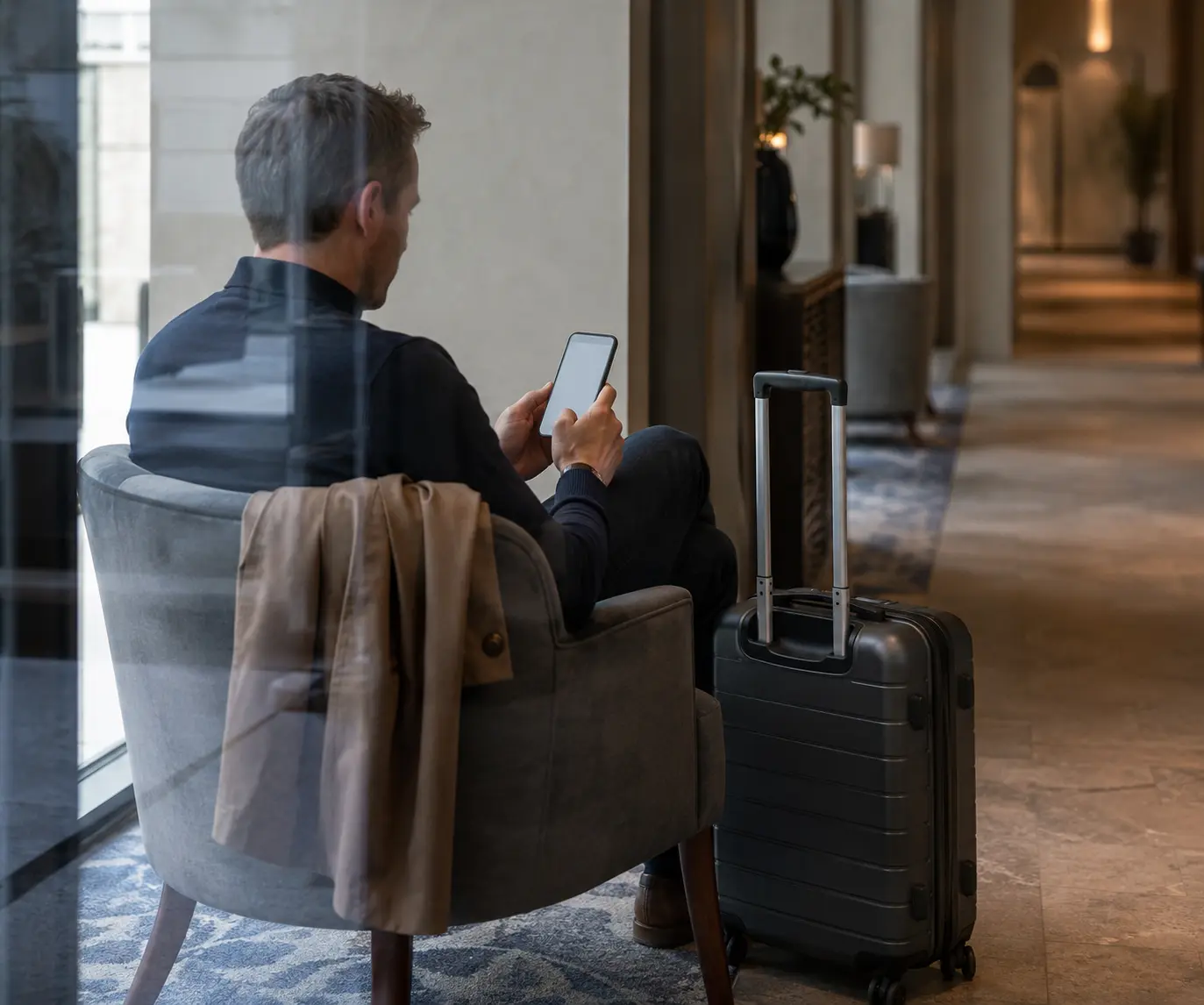 Traveller checking a phone while seated beside luggage in a hotel lobby