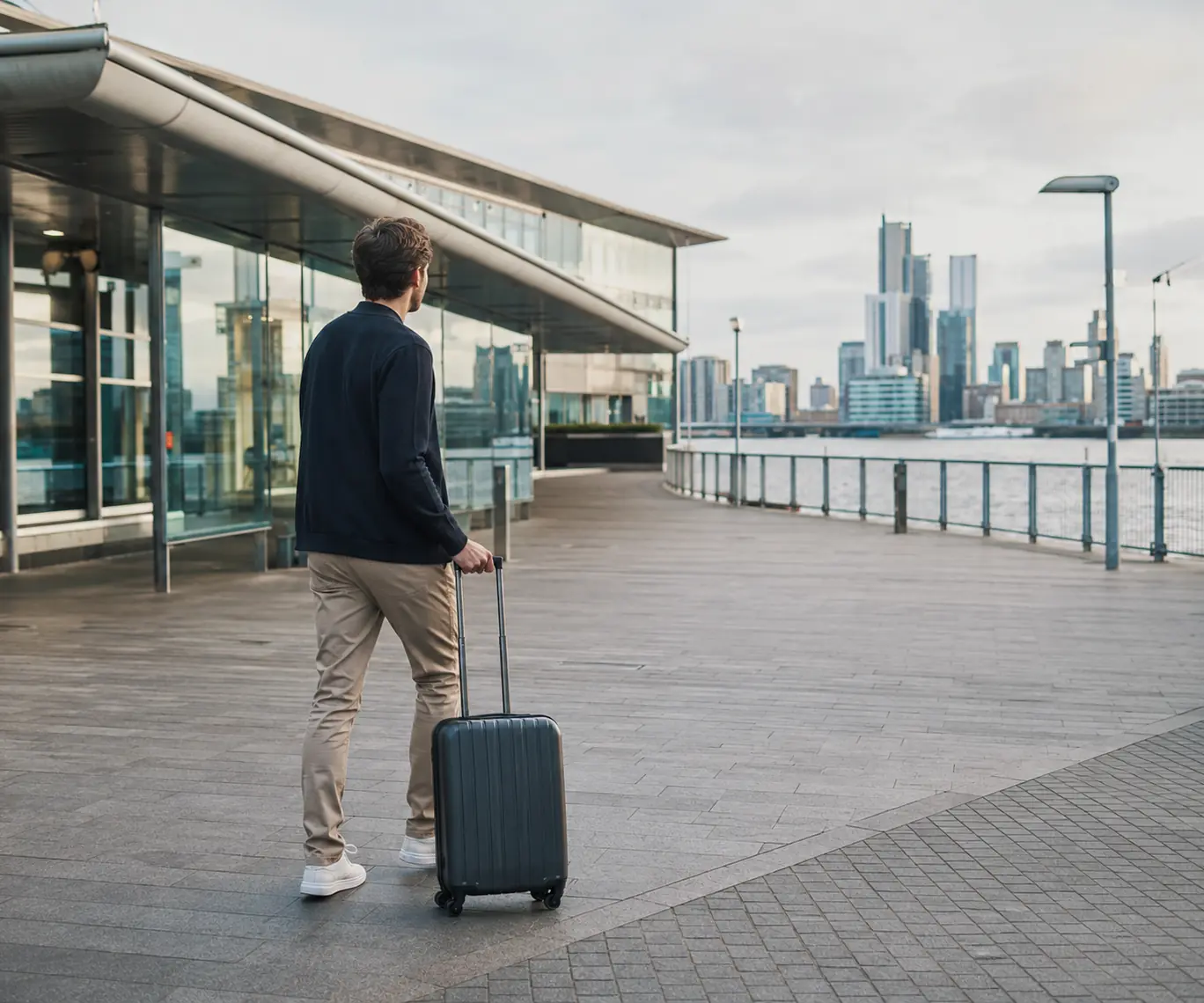Business traveller walking with a cabin suitcase beside a modern waterside airport building